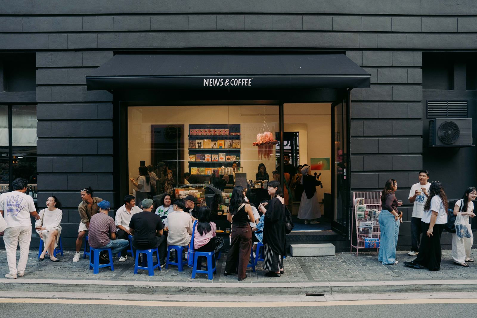 The News & Coffee pop-up in Kuala Lumpur: a full street terrace on blue stools outside the shop.